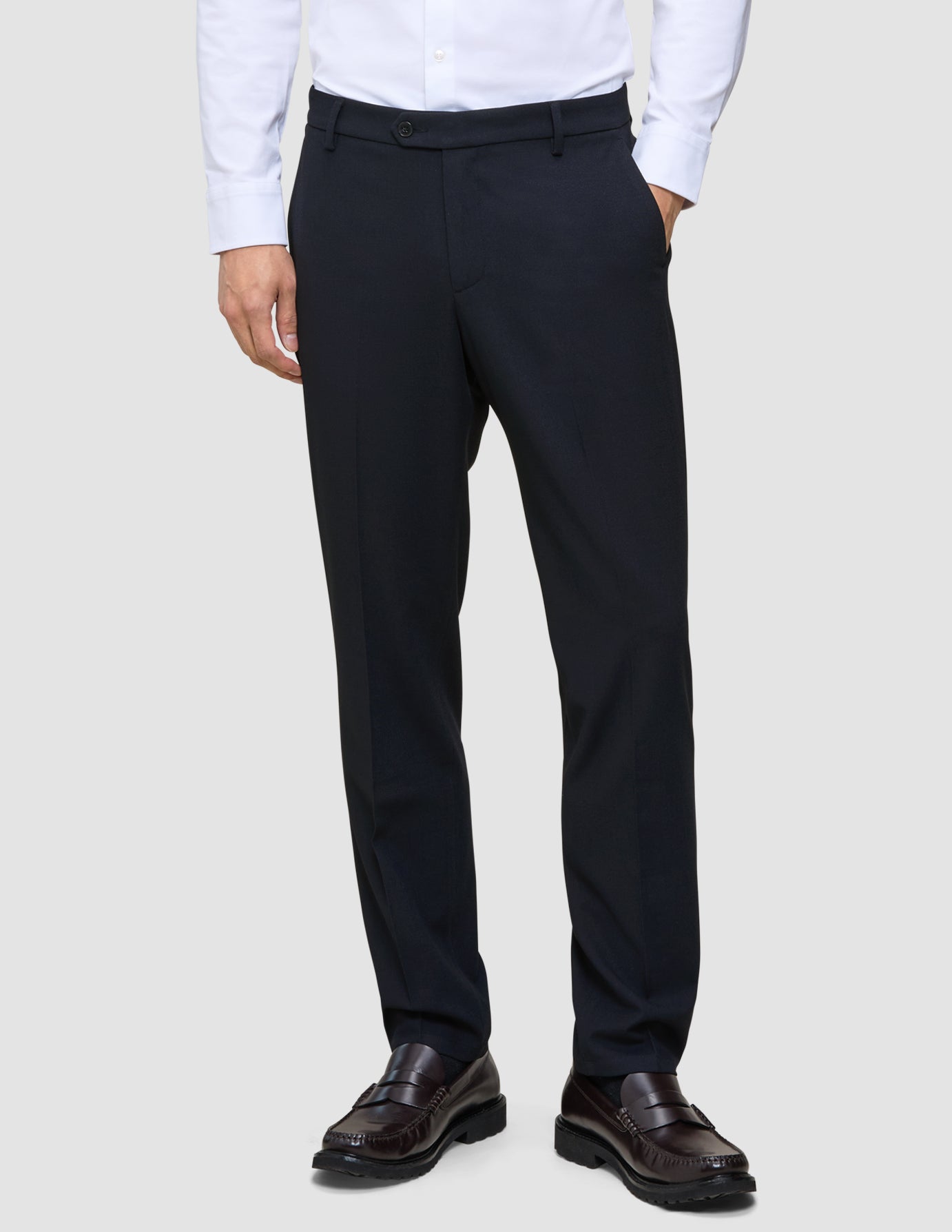En person klädd i Motion Suit-byxor i storlek Regular i färgen Midnight Blue, en vit skjorta med knappar och mörka läderskor av typen loafers.